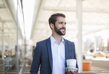 Lächelnder junger Geschäftsmann hält Tablett mit Kaffee zum Mitnehmen - DIGF04084