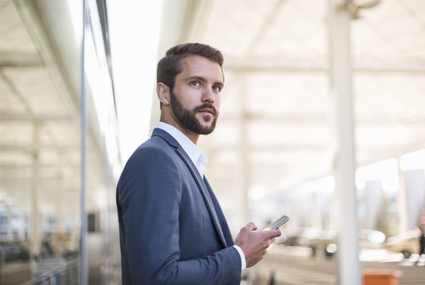 Junger Geschäftsmann hält Handy und schaut zur Seite, lizenzfreies Stockfoto