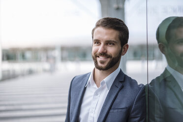 Portrait of smiling young businessman at glass facade - DIGF04098