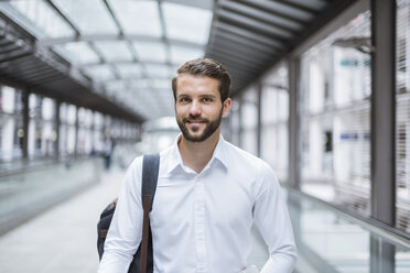 Portrait of smiling young businessman on moving walkway - DIGF04104