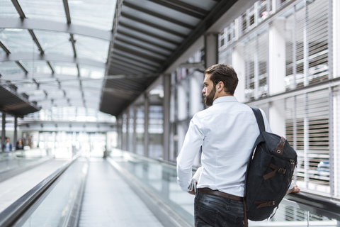 Young businessman with backpack on moving walkway stock photo