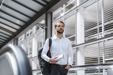 Young businessman with backpack and newspaper on the go - DIGF04108