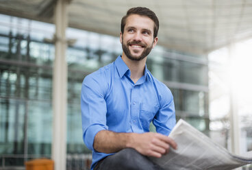 Lächelnder junger Geschäftsmann sitzt mit einer Zeitung im Freien - DIGF04118