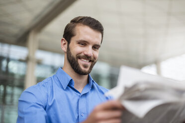 Lächelnder junger Mann liest Zeitung im Freien - DIGF04119