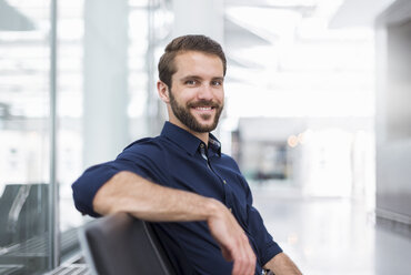 Portrait of smiling young businessman sitting in waiting area - DIGF04124
