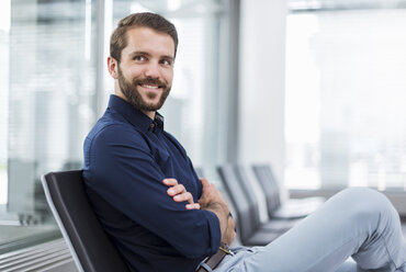 Smiling young businessman sitting in waiting area - DIGF04127