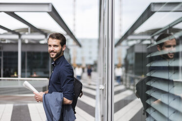 Smiling young businessman standing outdoors holding newspaper - DIGF04129