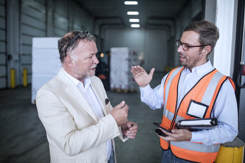 Businessman and man in reflective vest talking in industrial hall - ZEF15404
