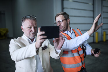 Mann in reflektierender Weste im Gespräch mit Geschäftsmann mit Mobiltelefon in Industriehalle - ZEF15405