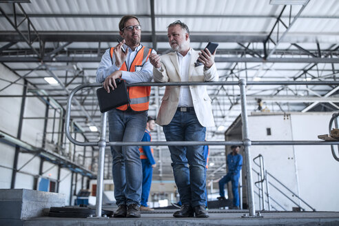 Man in reflective and businessman with cell phone talking in industrial hall - ZEF15407