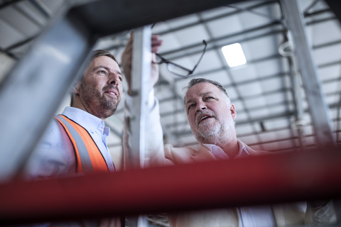 Businessman and man in reflective vest talking in industrial hall stock photo