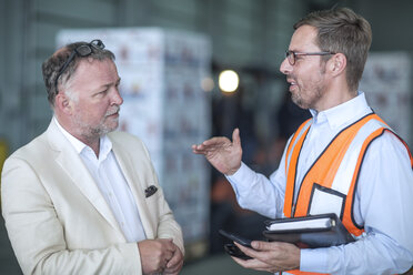 Geschäftsmann und Mann mit reflektierender Weste unterhalten sich in einer Industriehalle - ZEF15410