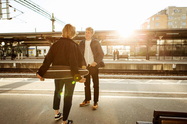 Happy young man talking with teenage girl while standing on railroad station platform - MASF07101