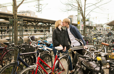 Young couple kissing while standing at bicycle parking station - MASF07106