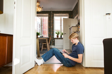 Side view of young man using digital tablet while sitting at doorway - MASF07110