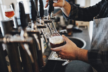 Mittelteil eines Barkeepers, der ein Glas füllt, während er einen Zapfhahn im Restaurant benutzt - MASF07144