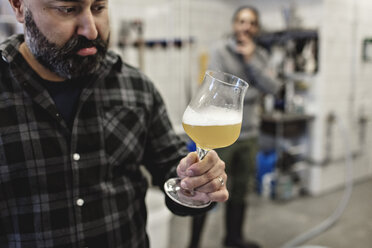 Selbstbewusster Manager, der ein Bier im Glas untersucht, während ein Mitarbeiter im Hintergrund steht - MASF07152