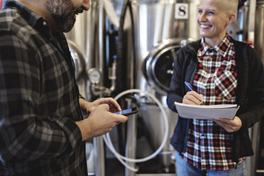 Smiling worker with spiral notebook discussing to male manager at brewery - MASF07169