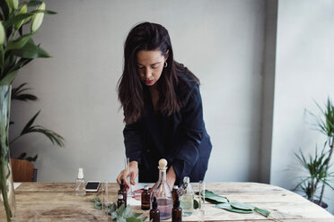 Mid adult female entrepreneur preparing perfume on table against wall at workshop - MASF07176