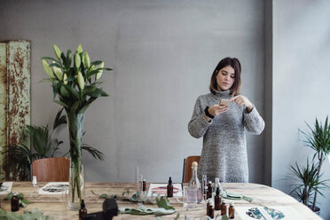 Eine erwachsene Frau fotografiert in einer Parfümwerkstatt verschiedene Flakons auf einem Tisch - MASF07179