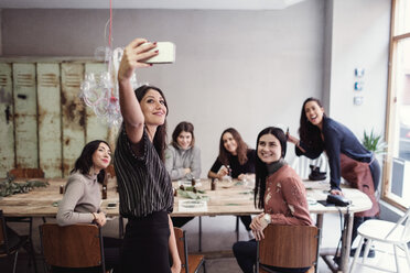 Smiling young woman taking selfie with female coworkers at table in workshop - MASF07206