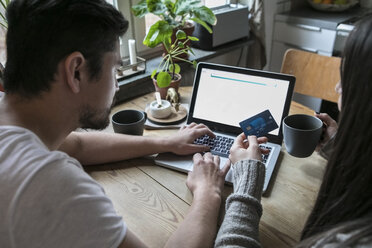 Couple having coffee and using credit card while shopping online through laptop at home - MASF07243