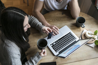 Blick von oben auf ein Paar, das Kaffee trinkt und eine Kreditkarte benutzt, während es zu Hause mit dem Laptop online einkauft - MASF07244