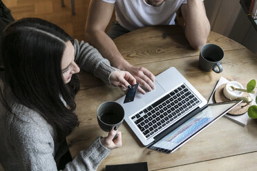 High angle view of couple having coffee and using credit card while shopping online through laptop at home - MASF07244