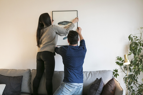 Paar hängt Gemälde auf und lehnt sich zu Hause auf dem Sofa an, lizenzfreies Stockfoto