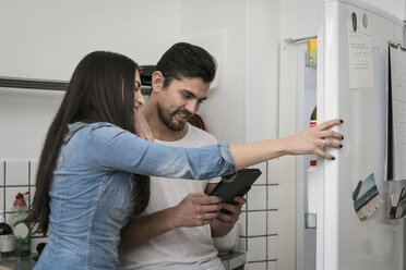 Lächelndes Paar, das ein digitales Tablet benutzt, während es in der Küche am Kühlschrank steht - MASF07251