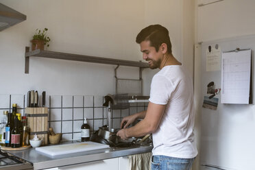 Smiling man washing utensils while standing by sink at kitchen - MASF07253