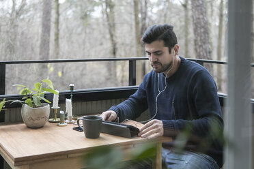 Man with headphones using digital tablet while sitting at table in balcony - MASF07259