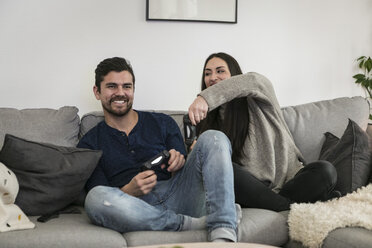 Happy couple enjoying while playing video game on sofa at home - MASF07260