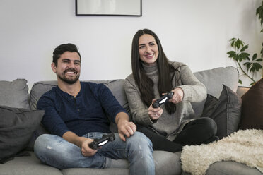 Happy couple playing video game while sitting on sofa at home - MASF07262