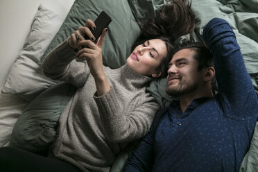 High angle view of smiling couple taking selfie through smart phone while lying on bed - MASF07266