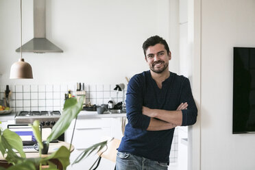 Portrait of smiling young man leaning on wall with arms crossed at home - MASF07279