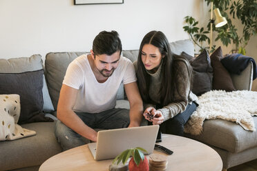 Couple using credit card while shopping online through laptop on sofa at home - MASF07284