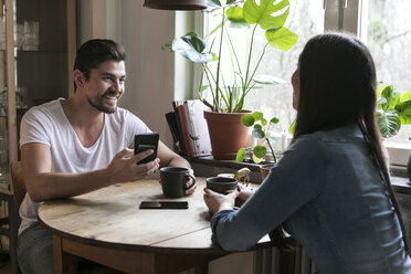 Lächelnder Mann mit Smartphone, der eine Frau bei einem Kaffee in der Küche ansieht - MASF07286