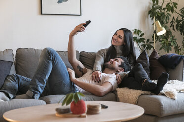 Lächelndes Paar, das ein Selfie mit dem Handy macht, während es sich auf dem Sofa zu Hause ausruht - MASF07287