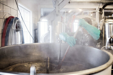 Arbeiter trägt Handschuh beim Umrühren von Bier im Container in einer Brauerei - MASF07293