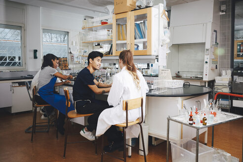 Multiethnische junge Universitätsstudenten sitzen auf Stühlen in einem Chemielabor - MASF07322