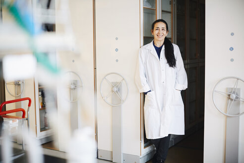 Portrait of confident mature female teacher standing with hands in pockets against storage cabinets in university - MASF07327