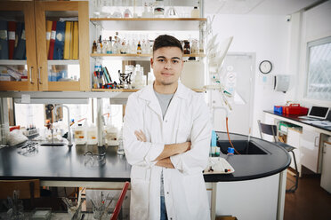 Porträt eines selbstbewussten jungen männlichen Studenten, der mit verschränkten Armen in einem Chemielabor steht - MASF07341