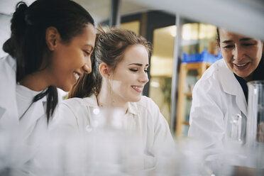 Happy mature teacher with young multi-ethnic female students learning at chemistry laboratory - MASF07361