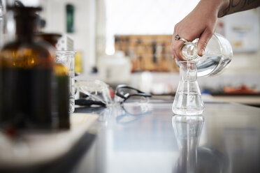 Abgeschnittene Hand einer Studentin, die eine flüssige Lösung aus einer Flasche im Labor in einen Kolben gießt - MASF07364