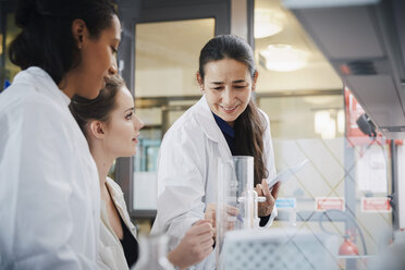 Smiling mature teacher with young female students learning chemistry at laboratory - MASF07365