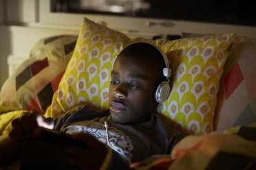 Close-up of boy with headphones using digital tablet while lying on bed at home - MASF07368