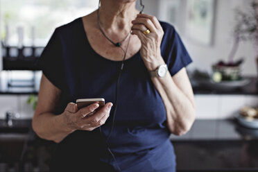 Mittelteil einer älteren Frau, die ein Smartphone in der Küche zu Hause hält - MASF07371