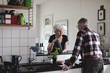 Ein älteres Ehepaar im Ruhestand steht am Küchentisch und diskutiert über ein digitales Tablet - MASF07372