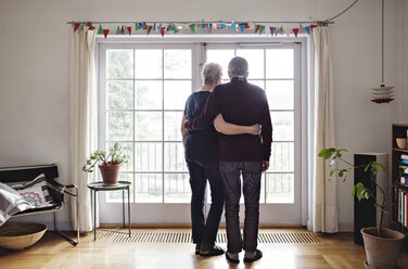 Rückansicht eines Ehepaars im Ruhestand in voller Länge, das durch das Fenster seines Hauses schaut - MASF07377